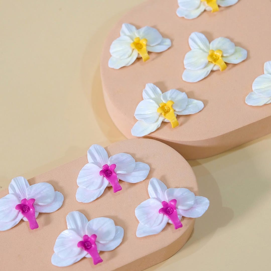 Orchid clay earring pieces in progress — white and magenta blooms on gold pin finding, ready to be assembled